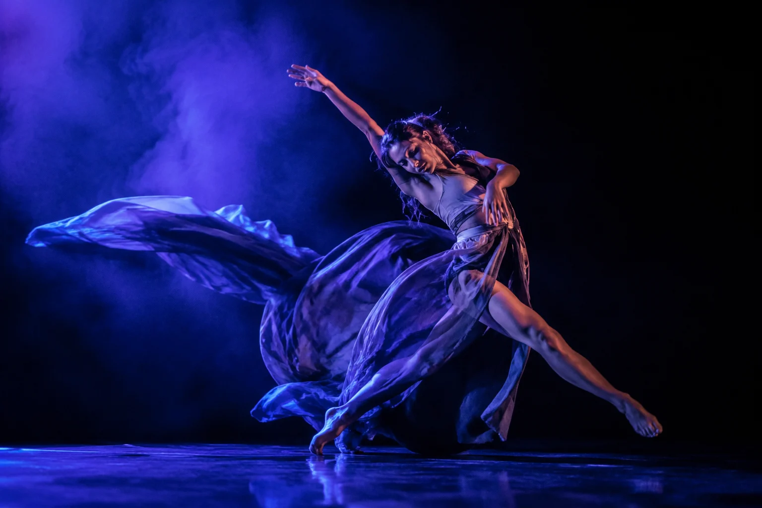 Bailarina contemporánea en movimiento bajo iluminación violeta y azul